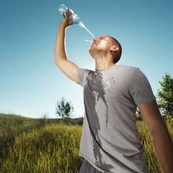 Signs of dehydration & heat exhaustion. Young man is refreshing himself with water from the bottle after workout in nature.