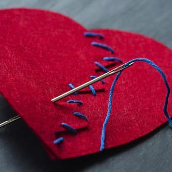 Broken heart sewn together with needle and thread