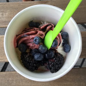 purple frozen yogurt in a bowl with blueberries and blackberries and a green spoon in it