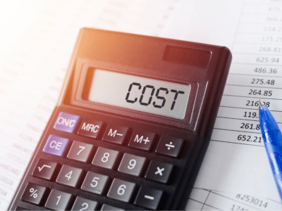 A close-up of a black calculator displaying the word 'COST' on its screen, placed on top of financial documents with various numerical figures. A blue pen is positioned next to the calculator, highlighting a section of the numbers. The image is brightly lit with a soft glow, emphasizing the concept of calculating expenses or costs