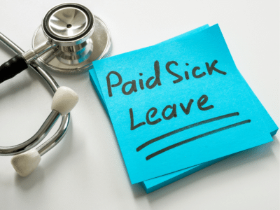 A close-up of a stethoscope next to a stack of blue sticky notes with 'Paid Sick Leave' written in bold black marker. The note is underlined, emphasizing the importance of paid sick leave in a healthcare or workplace context.