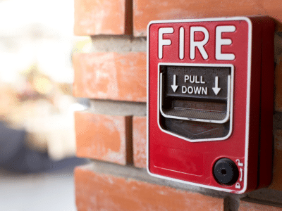 A red fire alarm switch mounted on a brick wall, with the words "FIRE" and "PULL DOWN" displayed.