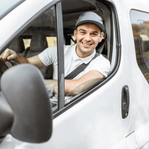 Smiling man wearing a cap sitting in the driver's seat of a white van.