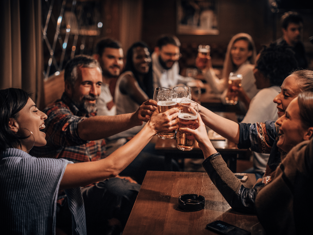 Group of people raising their glasses for a toast in a busy pub or restaurant.