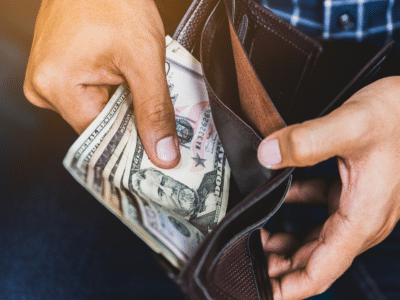 Close-up of a person holding cash from a wallet, representing out-of-pocket expenses Uber drivers may face without proper commercial insurance coverage.