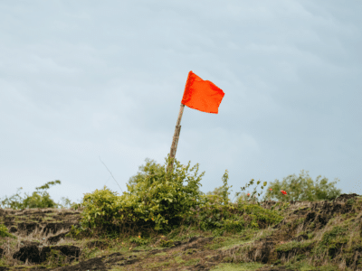 A bright red flag on a stick planted in a grassy landscape, symbolizing warnings or caution when selecting an insurance agent.