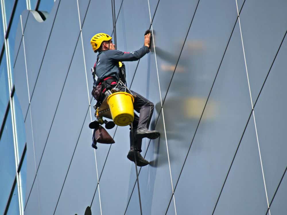 A window cleaner suspended on a harness, wearing a safety helmet and using professional equipment to clean a high-rise building.